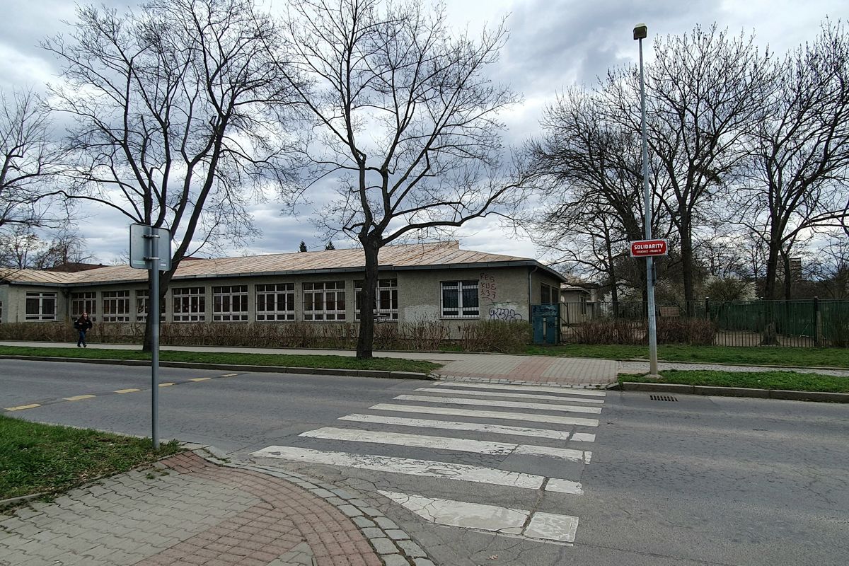 Nízké průčelí pavilonové školy z ulice Brigádníků s alejí stromů